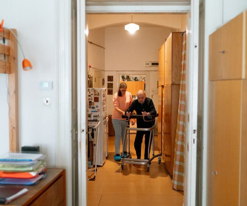 Pflegekraft begleitet einen älteren Menschen beim Gehen