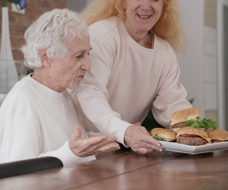 Pflegekraft hilft einem Patienten am Esstisch bei der Mahlzeit